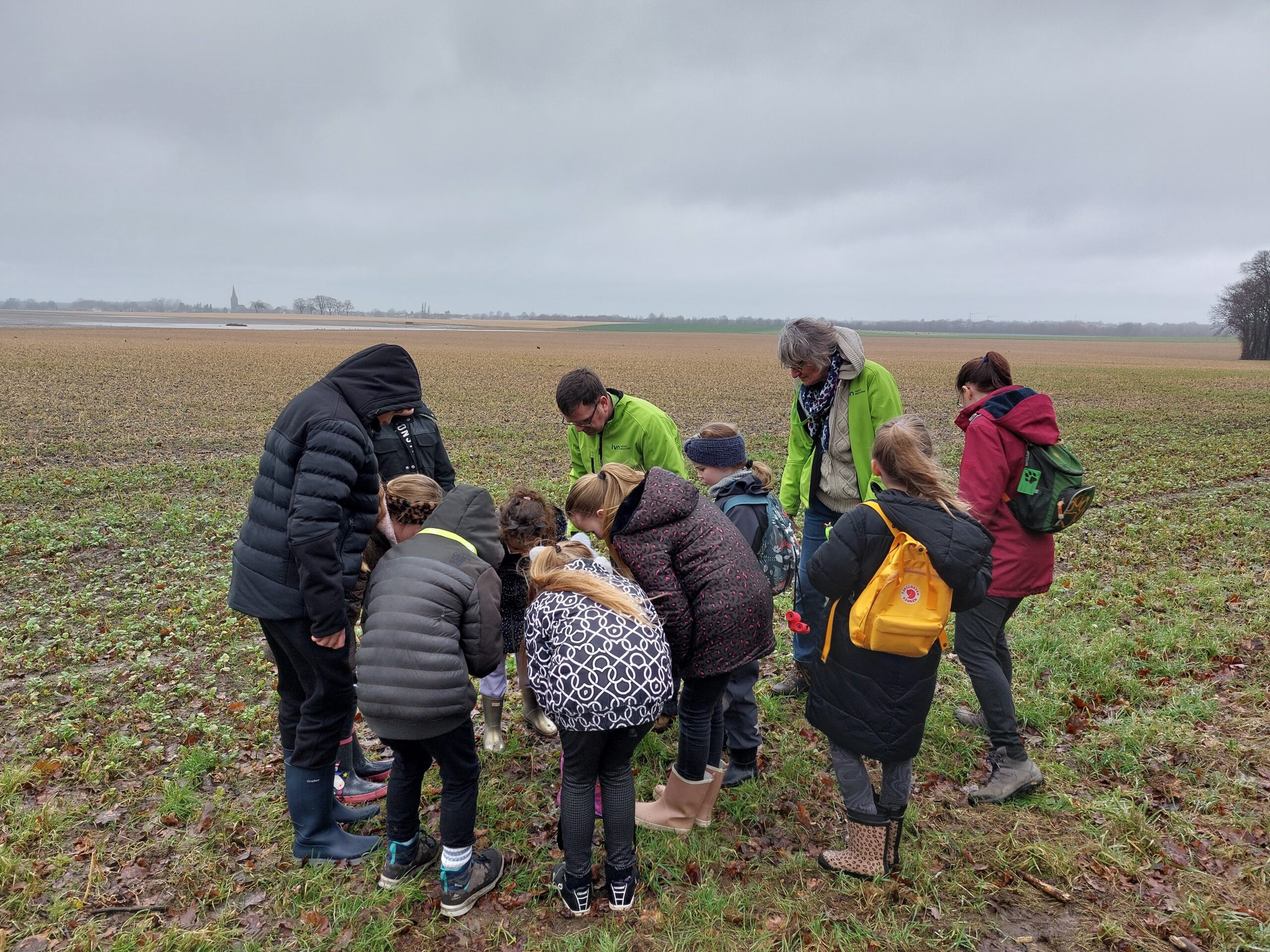Een groep mensen buigt zich over grasland onder een grijze, bewolkte hemel.