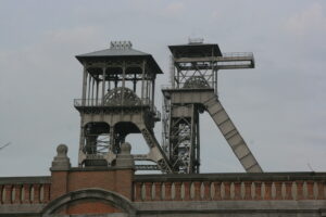 Historische mijnschacht met stalen koeltorens en bakstenen muur op de voorgrond.