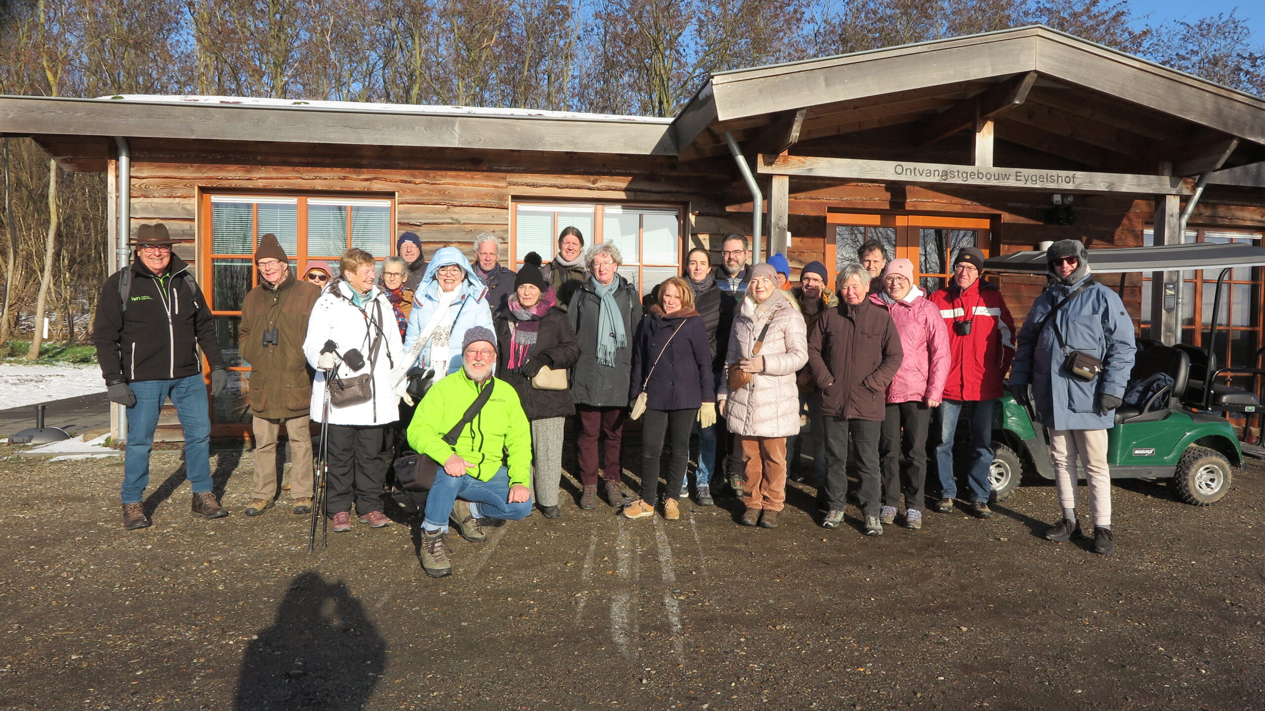 Groep mensen in winterkleding poseert voor een houten gebouw met bord "Ontvangstgebouw Eygelshof".