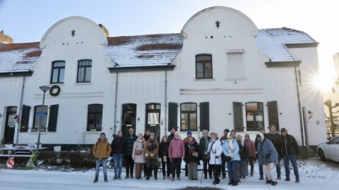 Groep mensen poseert voor een wit, historisch gebouw in een besneeuwd landschap met zonneschijn.