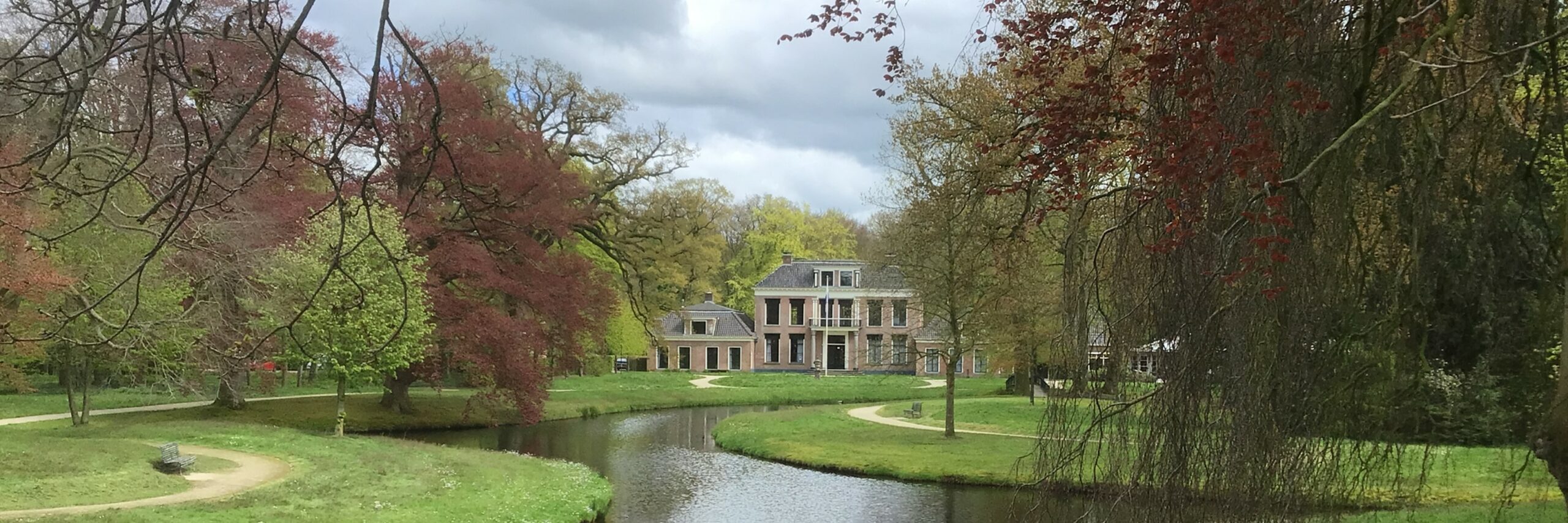 Landhuis omgeven door groene en rode bomen met een kronkelende vijver en paden.