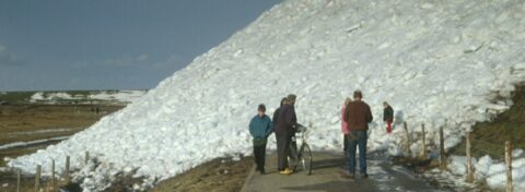 Mensen staan op een pad naast een grote heuvel van sneeuw.