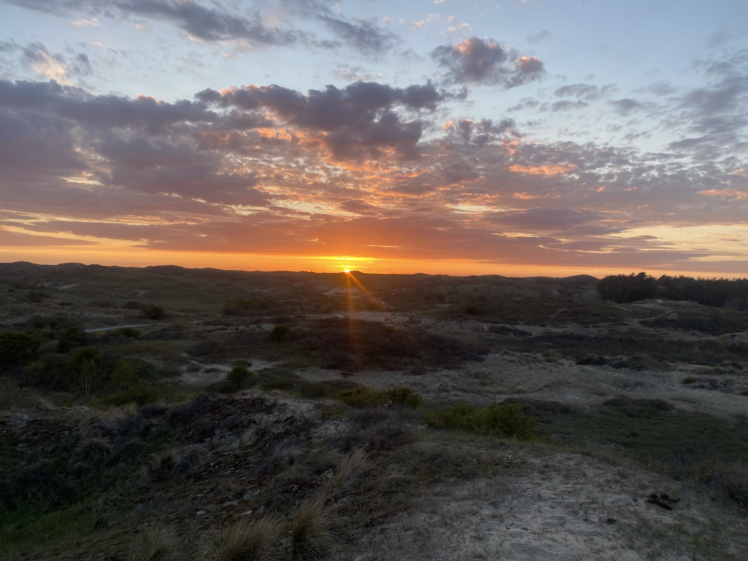 Zonsondergang boven een heuvelachtig landschap met kleurrijke wolken.
