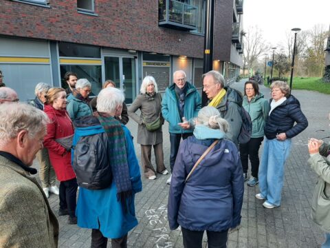 Een groep mensen verzameld bij een gebouw, mogelijk tijdens een rondleiding.