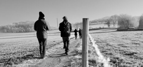 Wandelaars op een smal pad in een besneeuwd, heuvelachtig landschap.