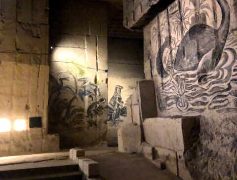 Muurtekeningen in een grot tonen dinosaurussen en waterelementen, een dino in een rivier.