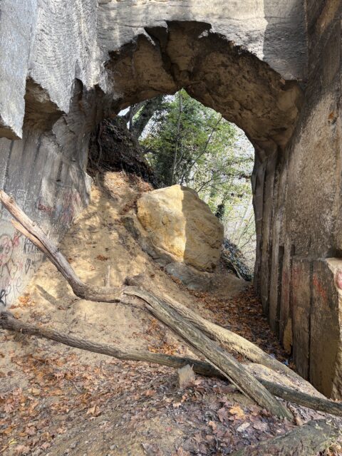 Oude tunnel met graffiti, gevallen takken en grote rots onder de boog, omringd door bomen.