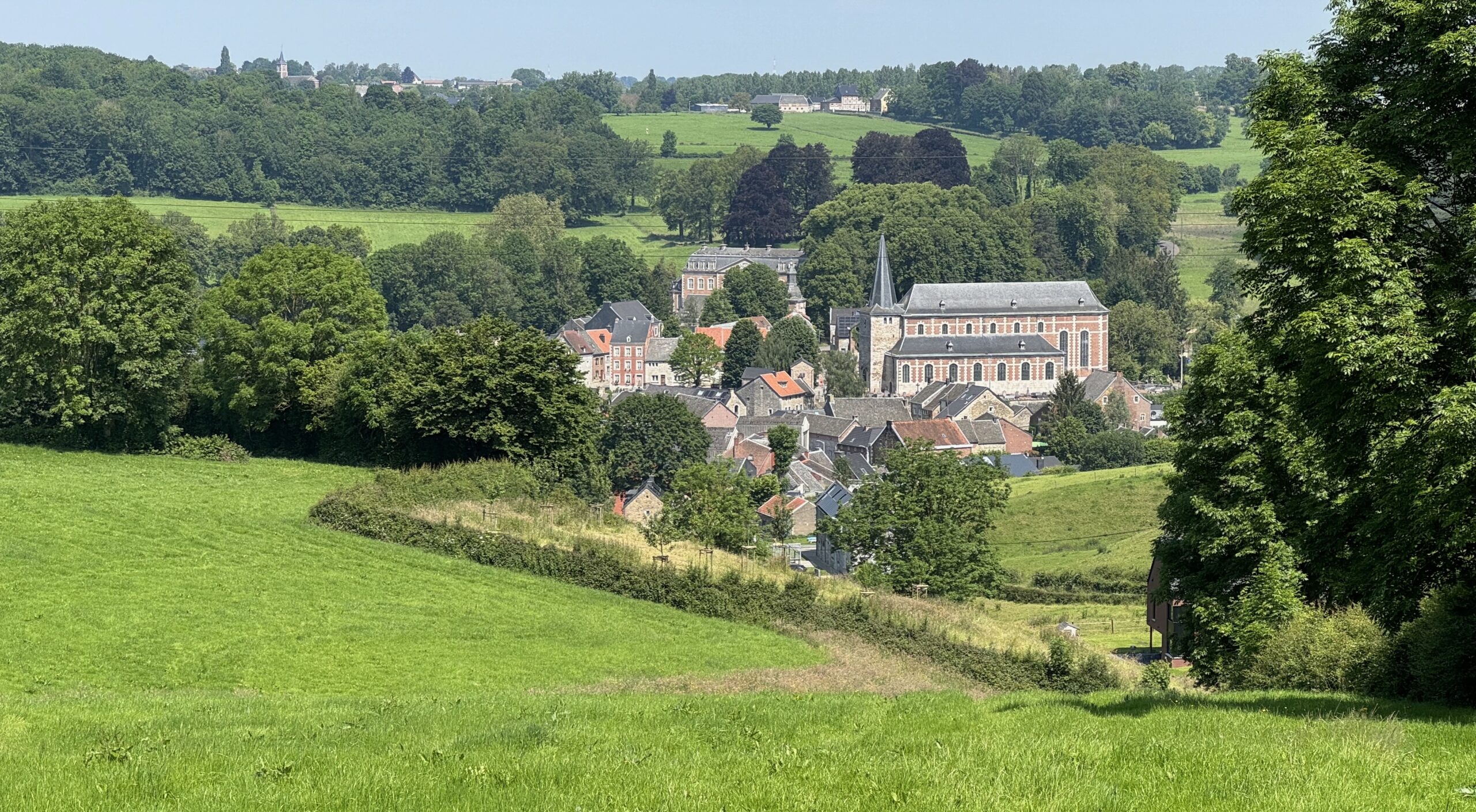Kerk omringd door historische gebouwen, te midden van groen heuvelachtig landschap.