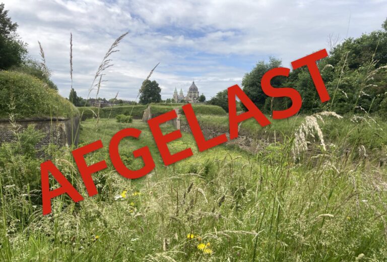 Groene tuin met ruïne en kerk op de achtergrond; rood 'AFGELAST' over het beeld.