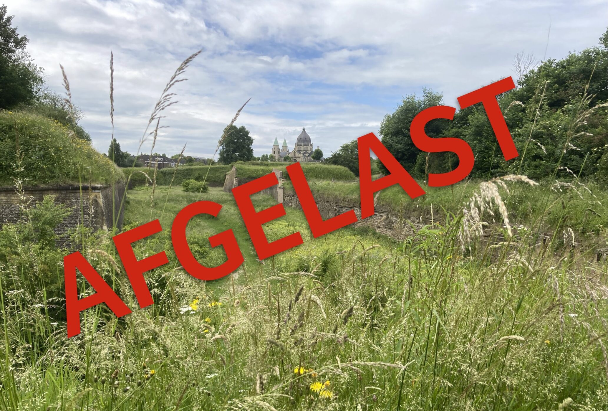 Groene tuin met ruïne en kerk op de achtergrond; rood 'AFGELAST' over het beeld.
