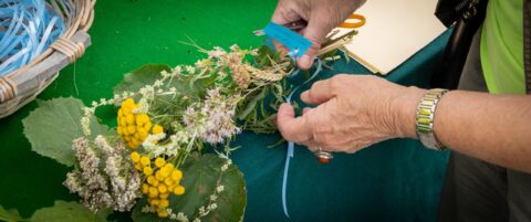 Handen binden bloemen en bladeren met blauw lint op groene tafel.