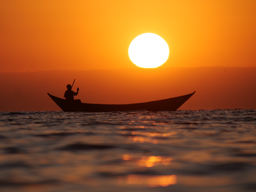 Silhouet van een kanoër bij zonsondergang op een stil meer.
