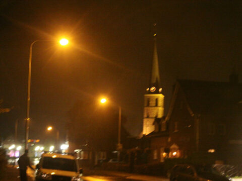 Nachtelijk straatbeeld met verlichte kerk en lantaarns.