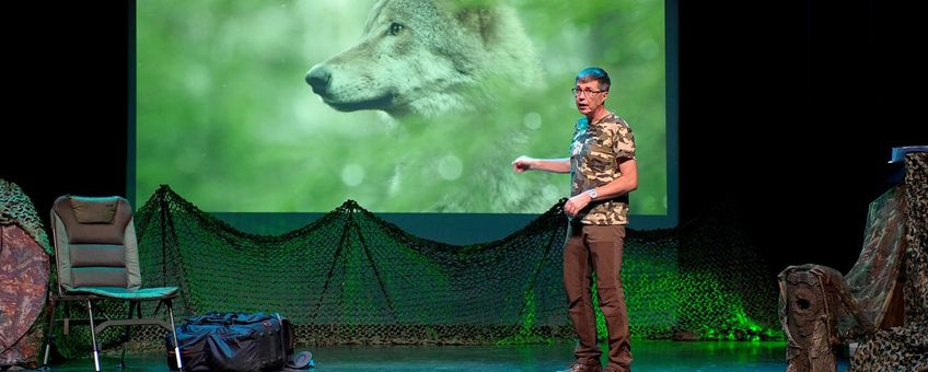 Man presenteert op podium met een afbeelding van een wolf op een scherm, omringd door camouflage.