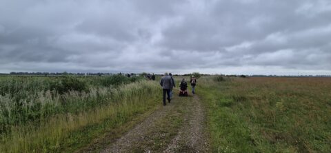 Een groep mensen wandelt over een landelijk pad onder een bewolkte hemel.