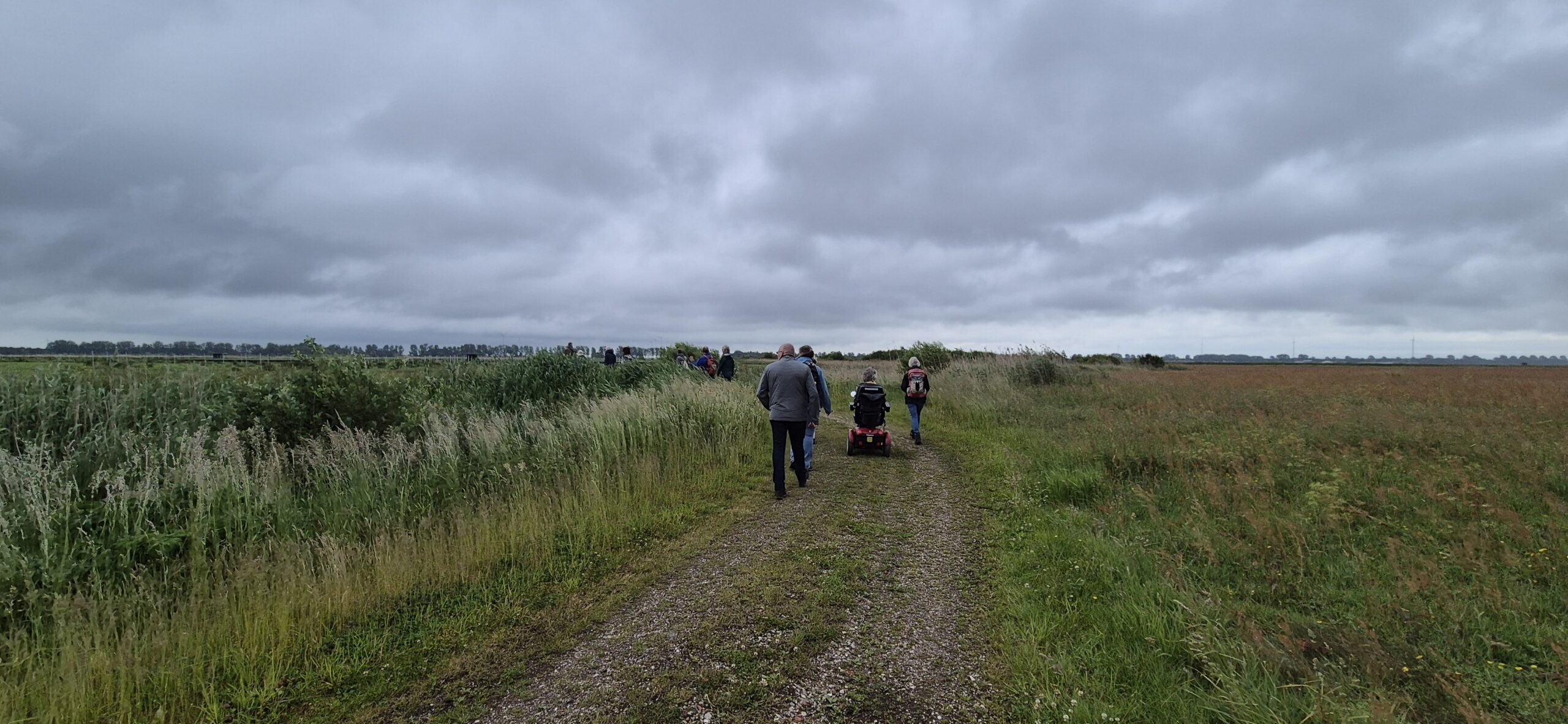 Een groep mensen wandelt over een landelijk pad onder een bewolkte hemel.