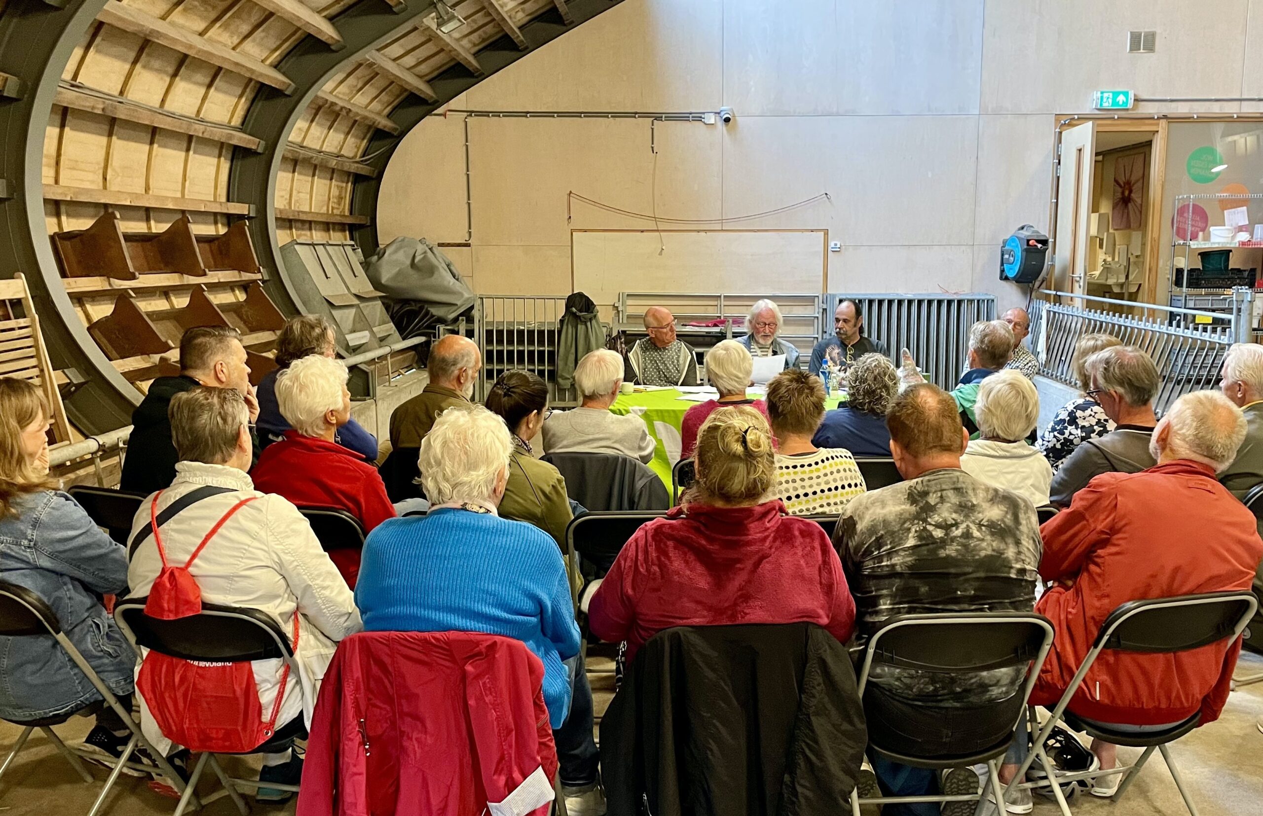 Groep mensen in een kring, luisterend naar panelleden in een moderne ruimte.
