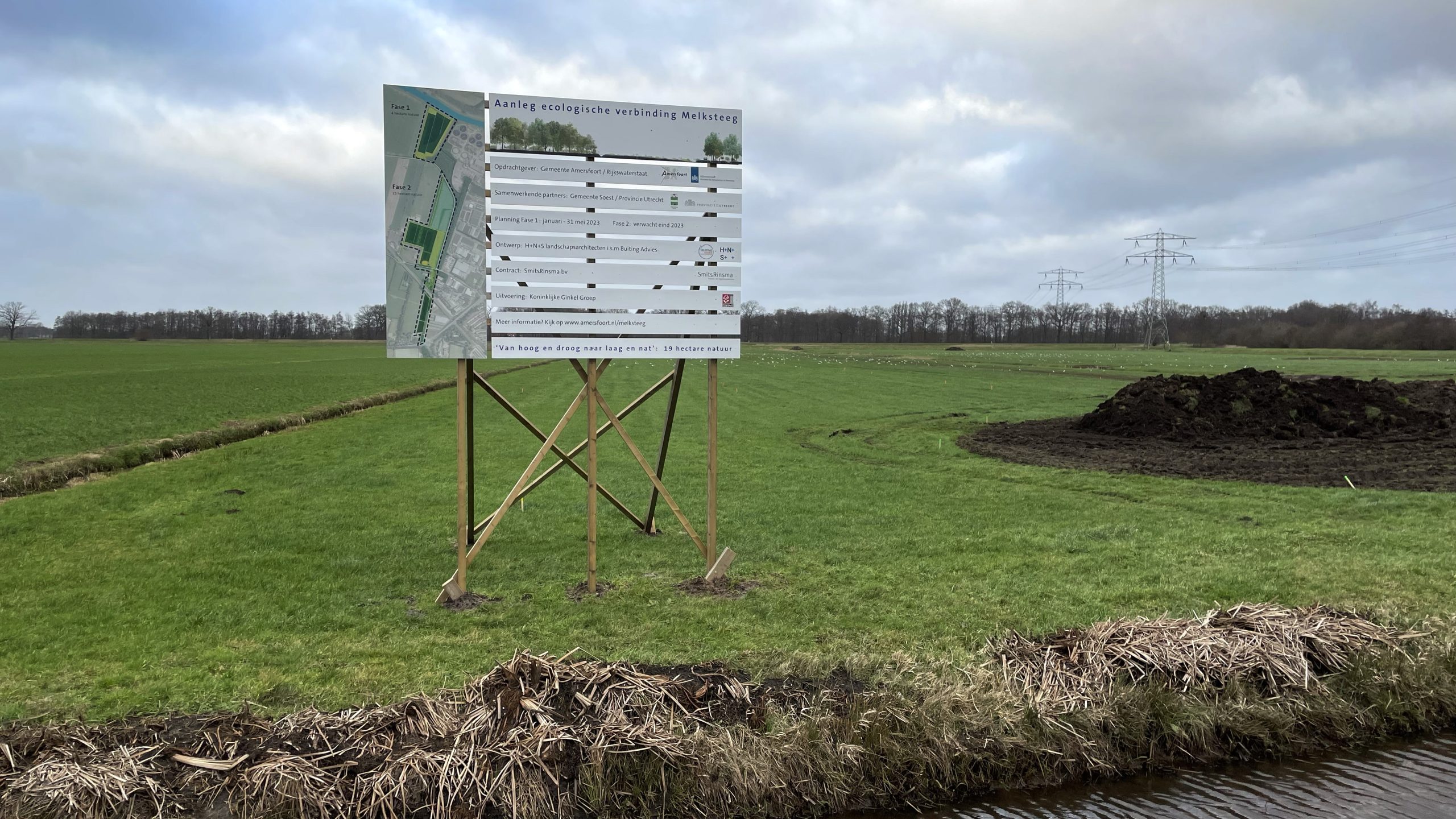 Bord bij weiland met tekst over ecologische verbinding Melksteeg; elektriciteitsmasten zichtbaar.