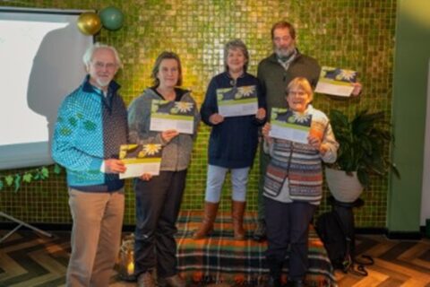 Vijf mensen poseren samen met certificaten voor een groene betegelde wand.
