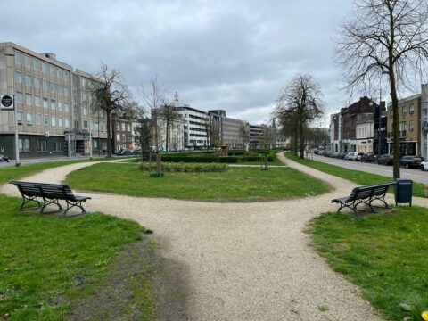 Stadspark met kronkelpaden, bankjes en kale bomen onder een bewolkte hemel.