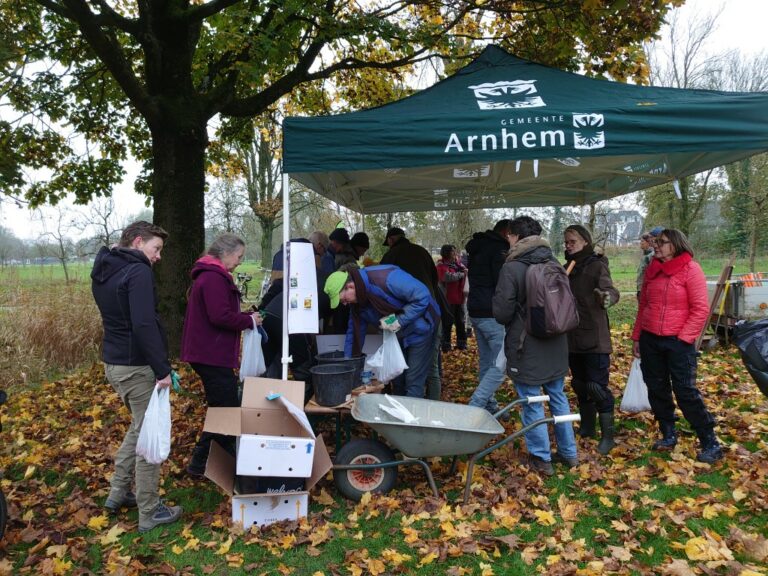 Mensen verzamelen zich onder een tent in een herfstlandschap, bezig met een tuinierevenement.