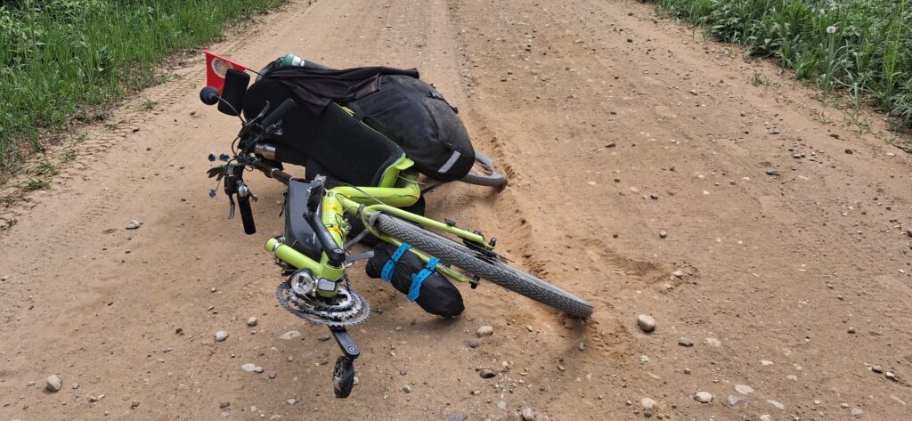 Ombgevallen ligfiets op zandweg met groene berm.