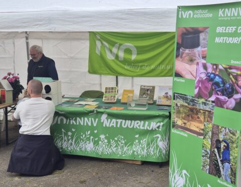 Informatietent over natuur met brochures en banners, begeleider praat met bezoekers.