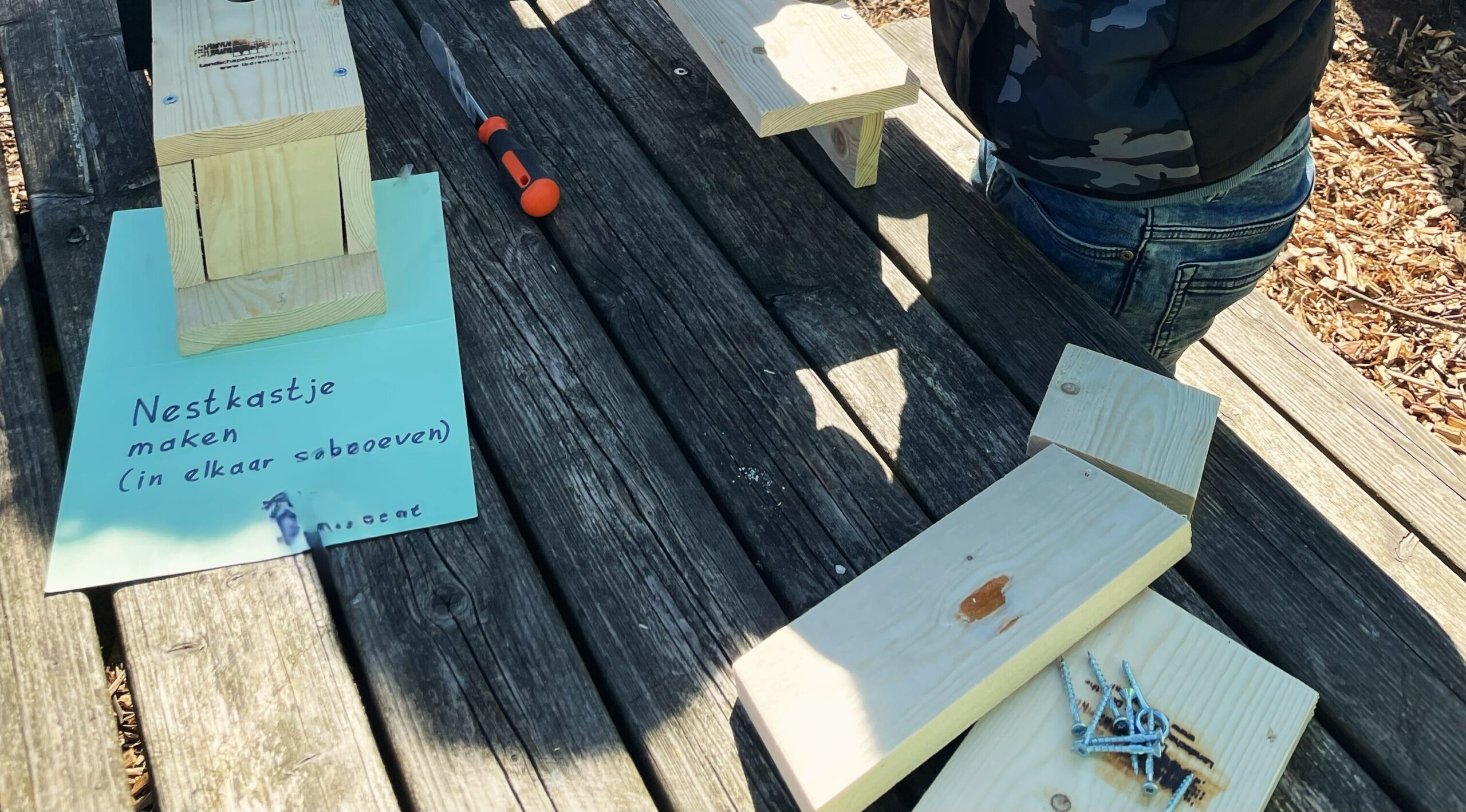 Houten onderdelen en schroeven voor het maken van een nestkastje op een houten tafel.