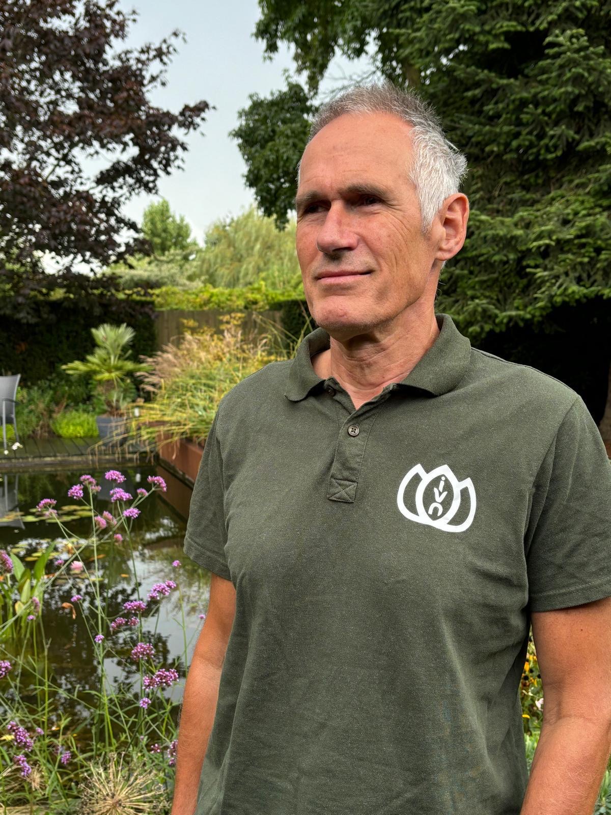 Man in groene polo staat voor een vijver in een groene tuin.