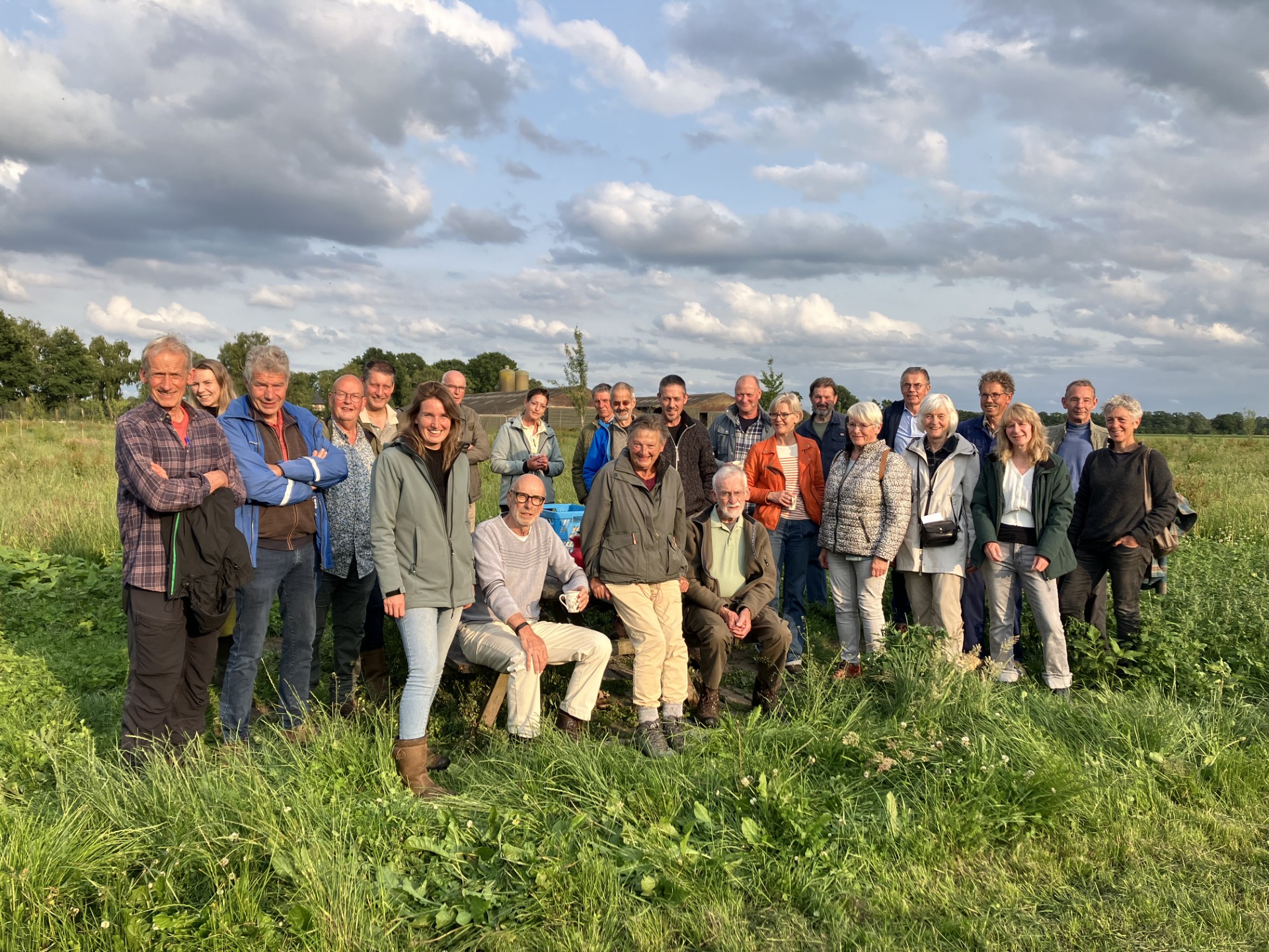 Groep mensen poseert buiten in een grasveld onder een bewolkte lucht.