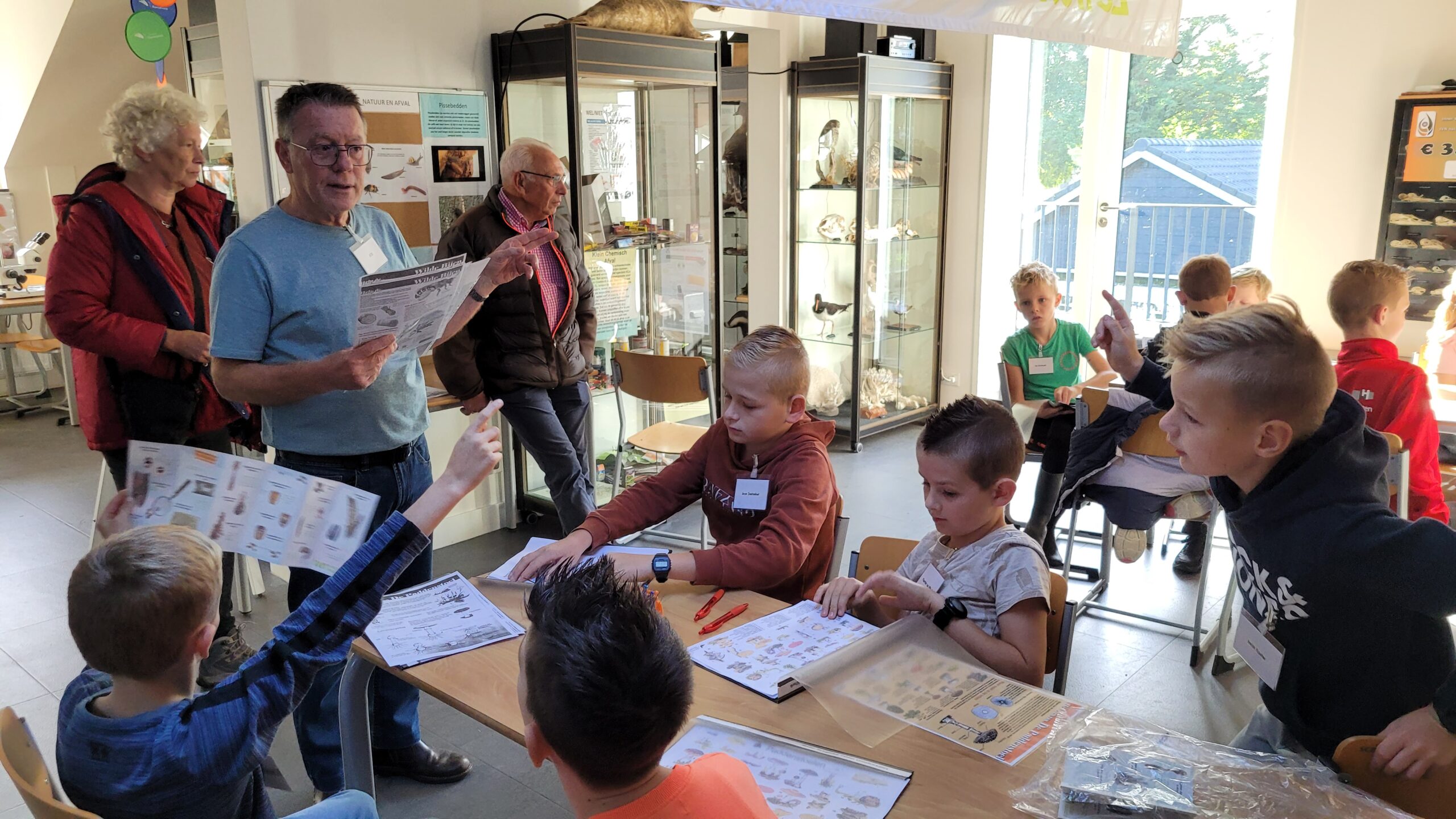 Mensen en kinderen zitten in een educatieve ruimte met gids en studiemateriaal rondom.