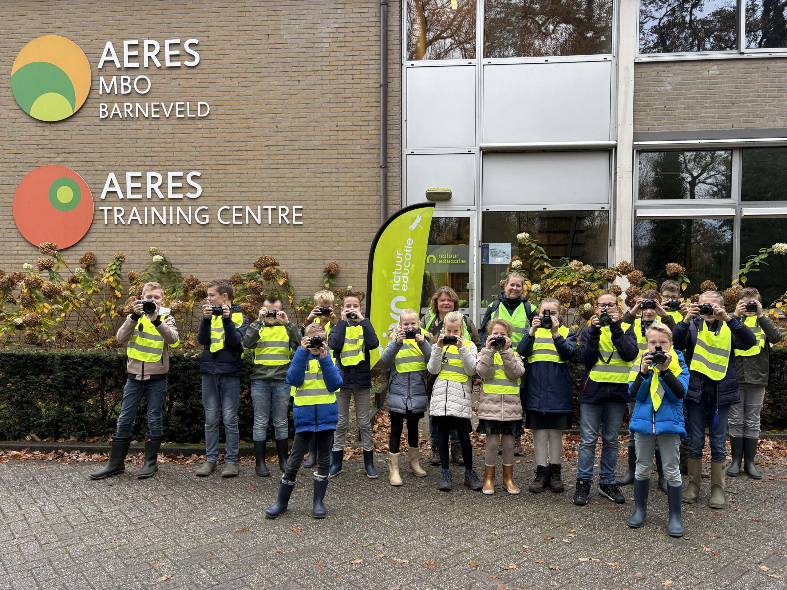 Groep kinderen met camera's en gele hesjes voor Aeres MBO Barneveld.