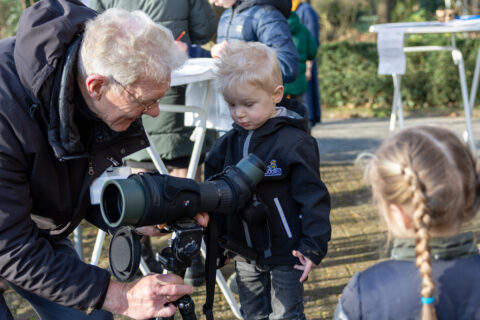 Ouder man leert jongetje door telescoop kijken in een buitenomgeving.