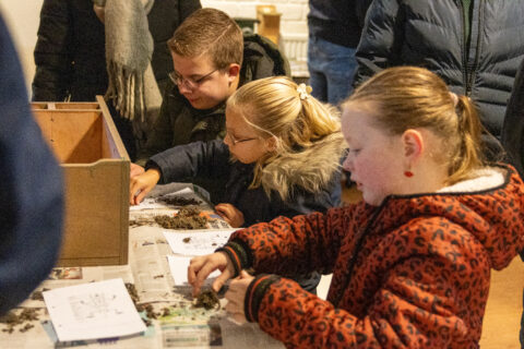 Kinderen knutselen met aarde en papier tijdens een binnenactiviteit aan een tafel.