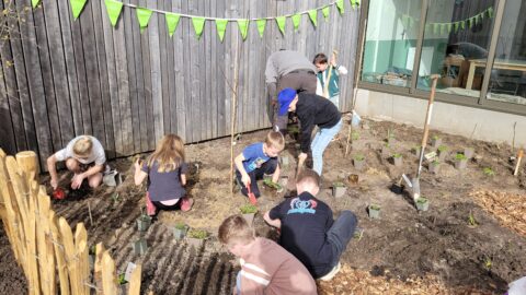 Kinderen planten jonge plantjes in een tuin met groene vlaggetjes boven hen.