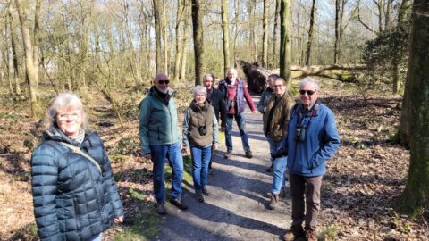 Groep mensen wandelt op een bospad, met verrekijkers om hun nek.