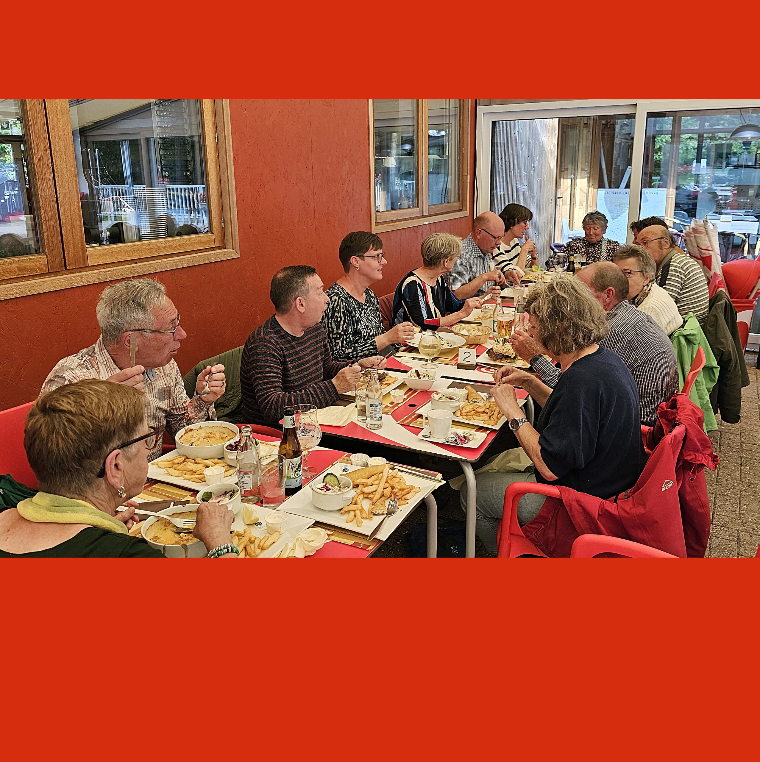 Groep mensen aan lange tafel in restaurant, genietend van een maaltijd samen.