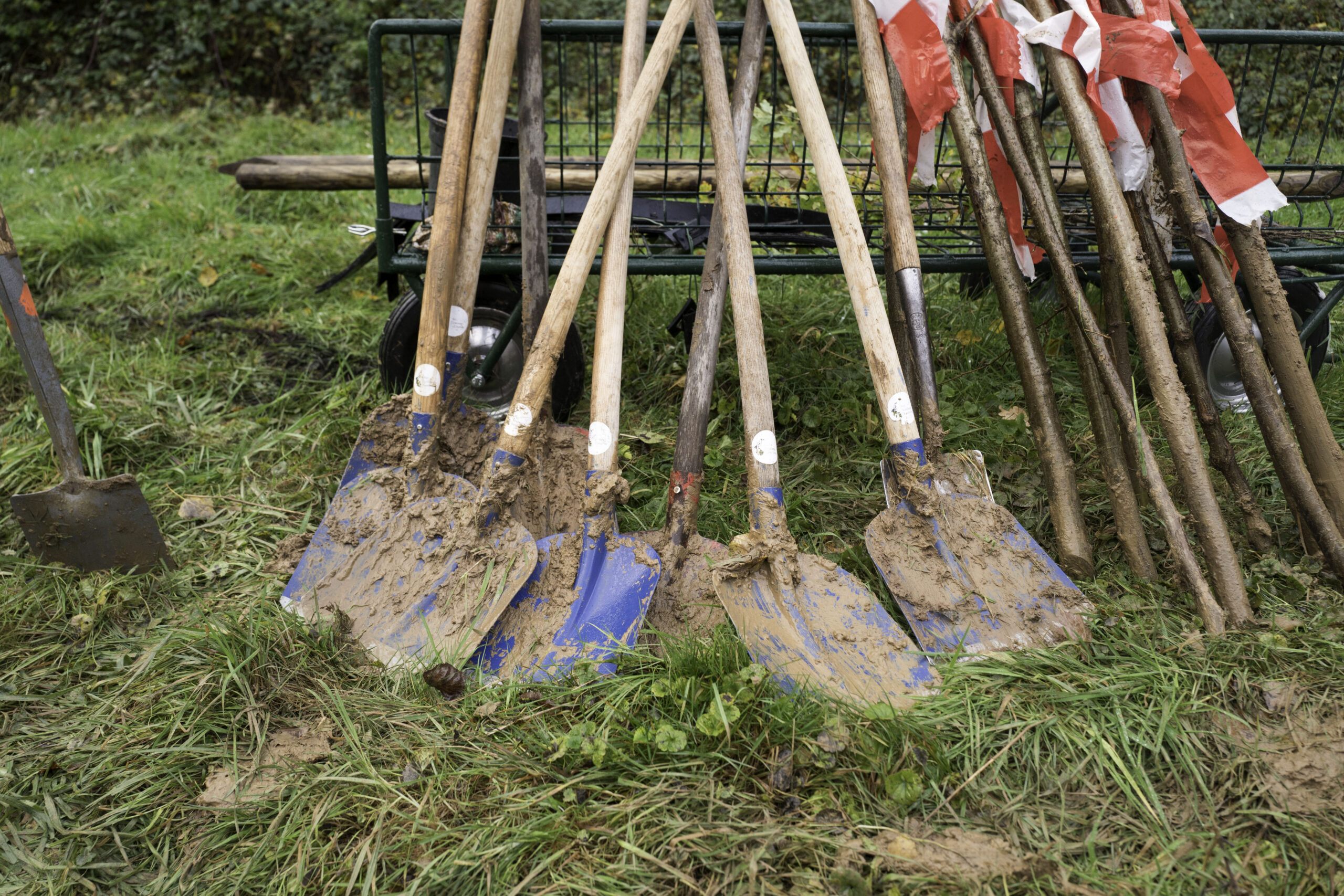 Muddy schoppen leunen tegen een kar op grasland, omringd door gereedschap.