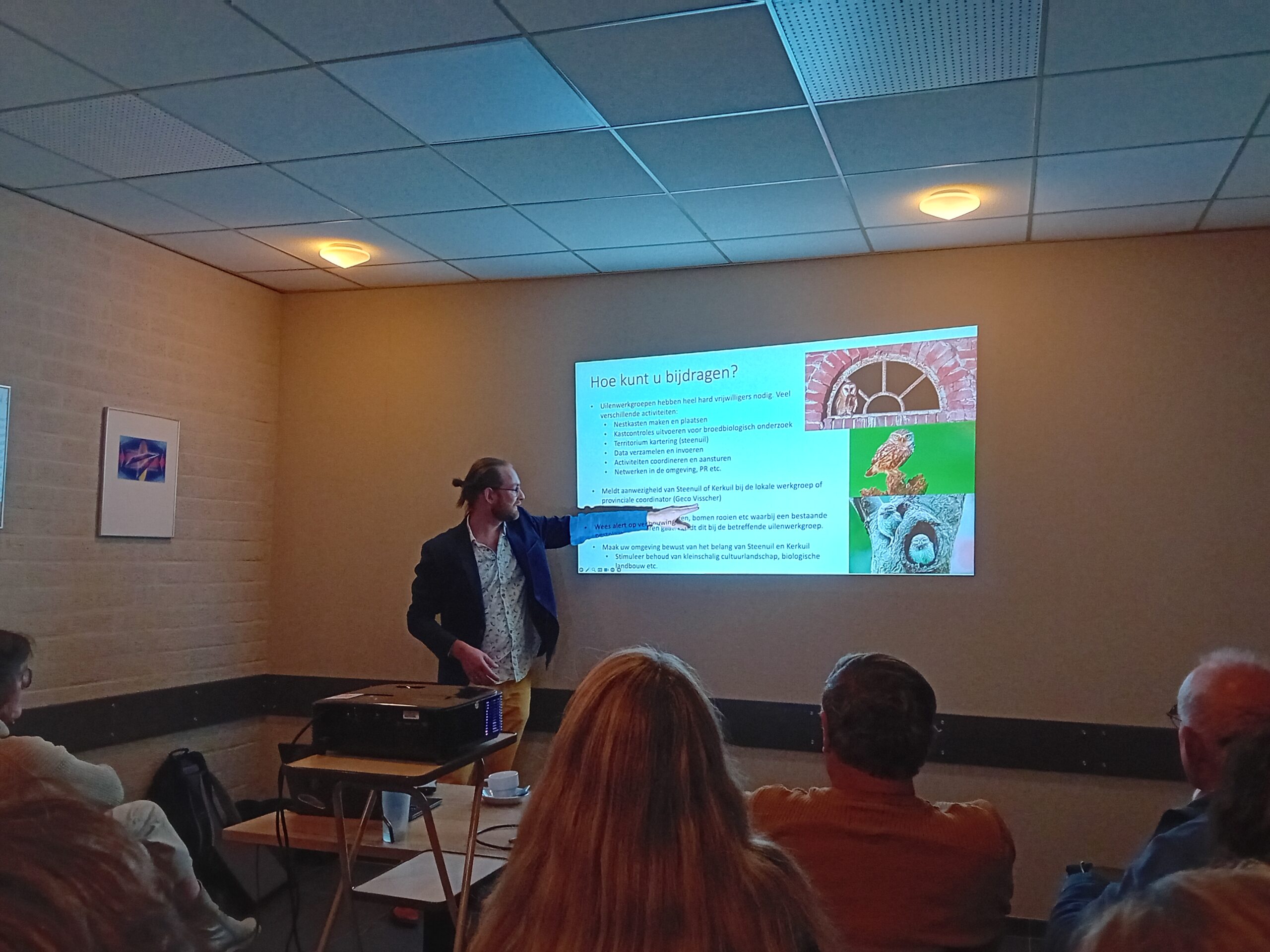 Man geeft presentatie in een vergaderruimte; een dia met tekst en natuurbeelden is geprojecteerd.