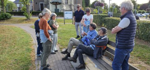 Groep mensen in gesprek in een park, sommigen zitten op een bank, anderen staan.