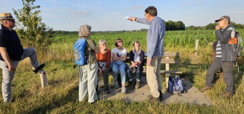 Groep mensen in gesprek op een bankje langs een pad in een groen landschap.