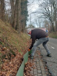 Man installeert een groen scherm langs een bladervrije weg in een bosachtige omgeving.
