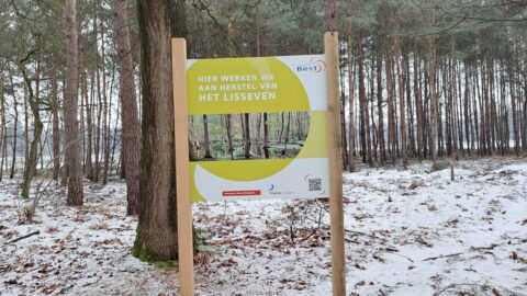 Een bord in een besneeuwd bos, over herstelproject Lisseven.