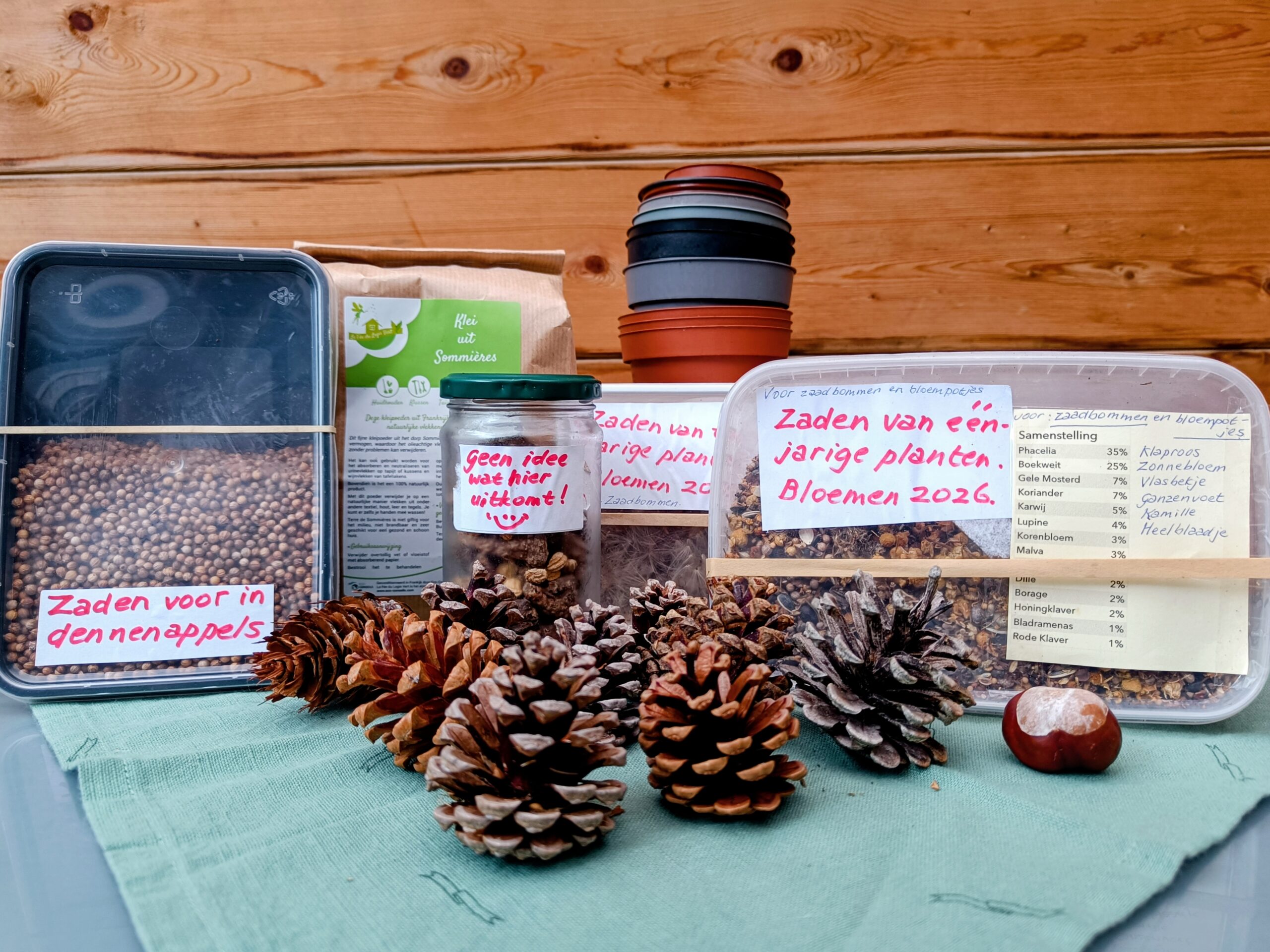 Zaadpotten, pijnappels en bloempotten op groene doek, met labels over zaden en tuindoelen.