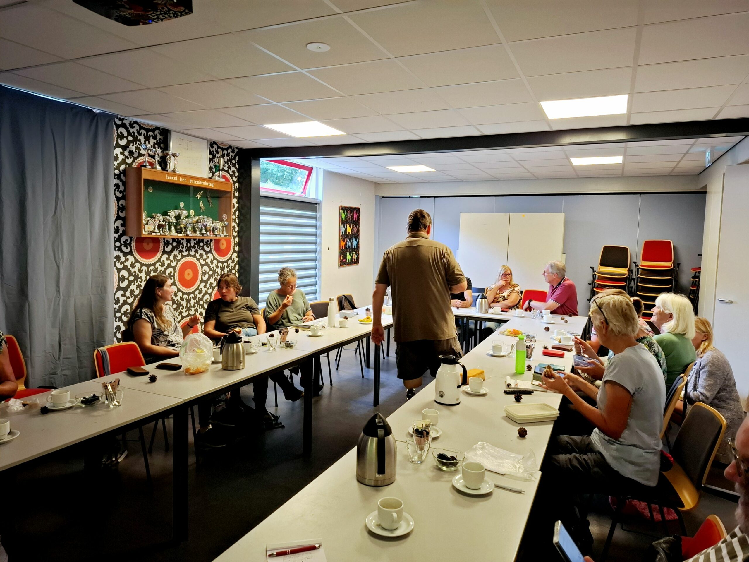 Groep mensen zit in een vergaderkamer aan een lange tafel met koffie en papier.