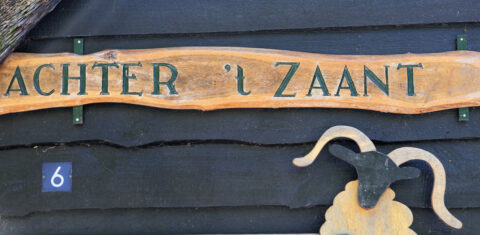 Houten bord met tekst "ACHTER 't ZAANT", naast blauw huisnummer 6 en een houten schapenhoofd.
