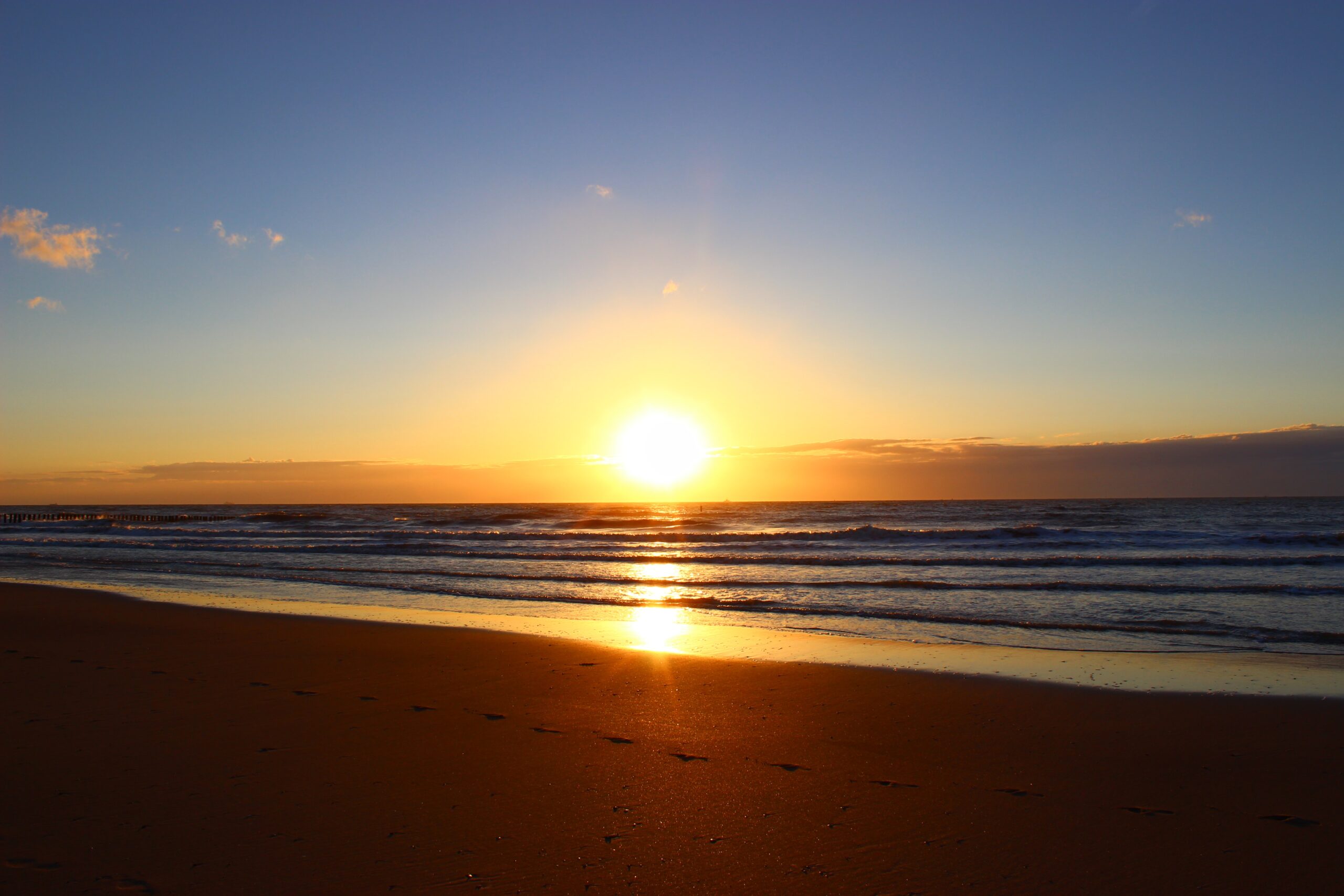 Zonsondergang boven een rustige zee met voetafdrukken in het zand op de voorgrond.