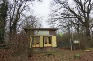 Een klein geel gebouw in een bos met een groene vlag aan de zijkant.