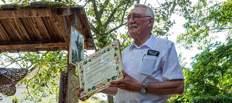 Een man in een witte blouse houdt een ceremonieel certificaat buiten vast.