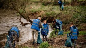 Mensen in blauwe hesjes ruimen afval op langs een rivier.